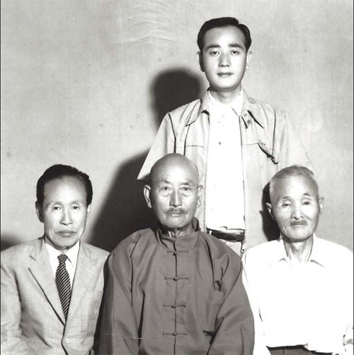 Kim Kwang Seok (em pé) sentado no meio Li Sui Tien.
